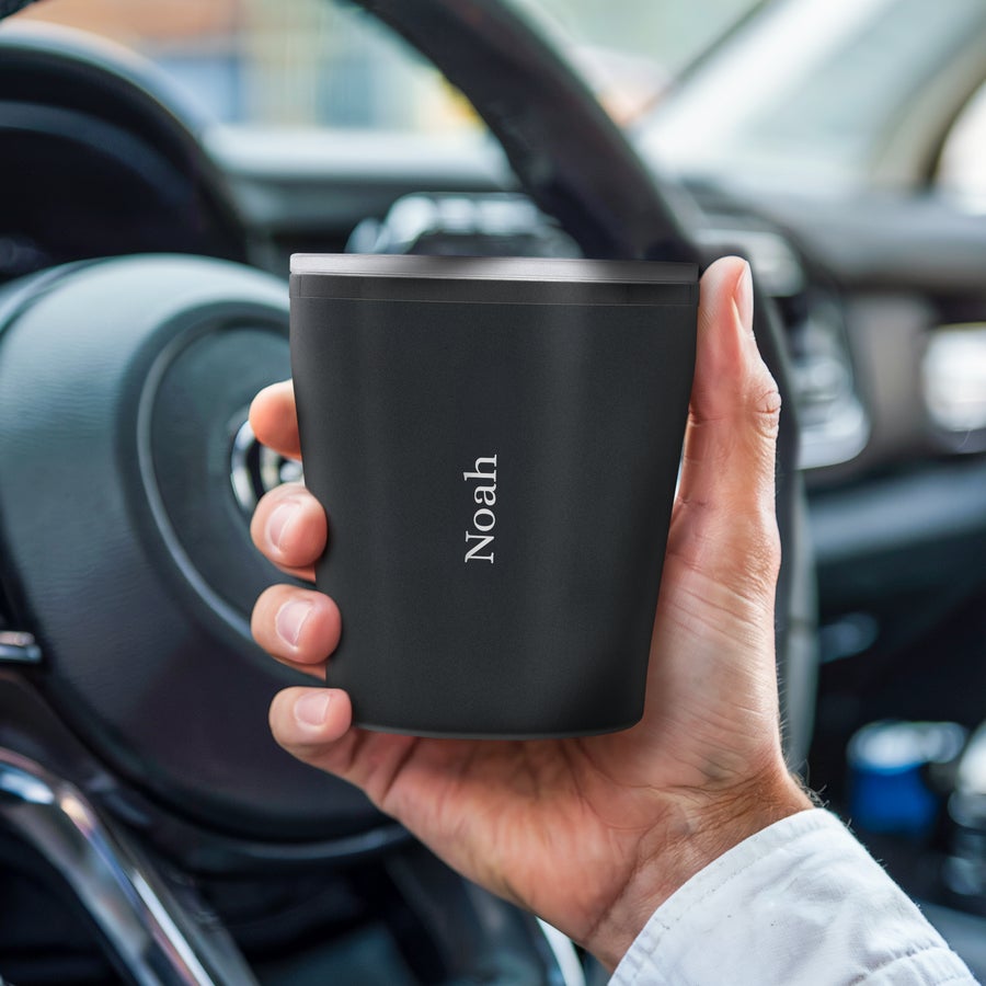 Hand holding a black personalized travel mug with the name Noah engraved, ready to sip in style.