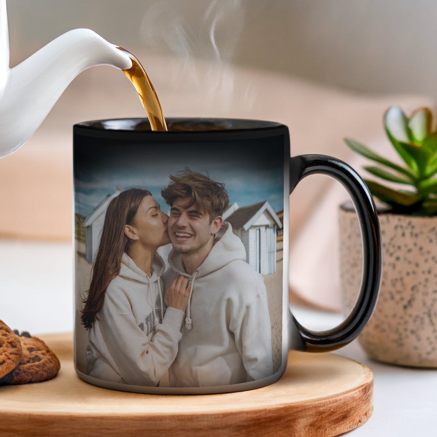 A black Personalised Mug - Magic with a custom printed photo of a couple on a beach, hot tea pouring in, making the image appear